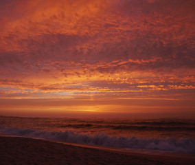 Vivid red sky at sunset on the beach with dark ocean