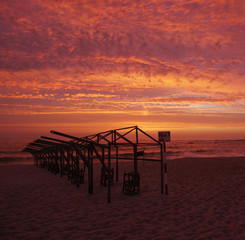 Beach hut frames silhouetted against vivid red sunset sky with dramatic clouds, on beach in Portugal