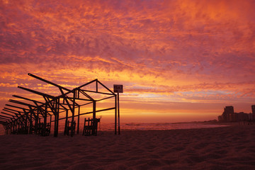 Beach hut frames silhouetted against vivid red sunset sky with dramatic clouds, on beach in Portugal