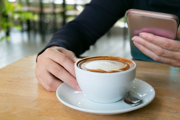Close-up image of woman take time at coffee shop with a cup of hot latte and her mobilephone.