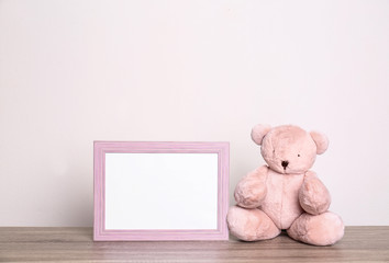 Photo frame and adorable teddy bear on table against light background, space for text. Child room elements