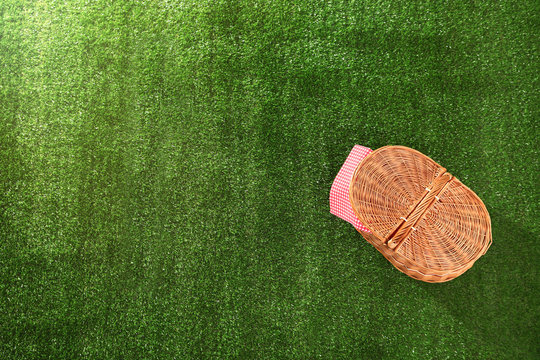 Closed picnic basket and napkin on grass, top view with space for text