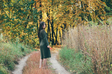 Dreamy beautiful girl with long natural black hair in sunlight on background with colorful leaves. Fallen leaves in girl hands in autumn forest. Female beauty portrait among vivid foliage in sunny day