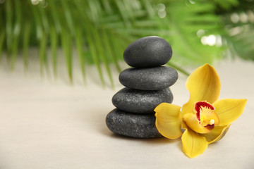 Stack of spa stones with flower on table against blurred background. Space for text
