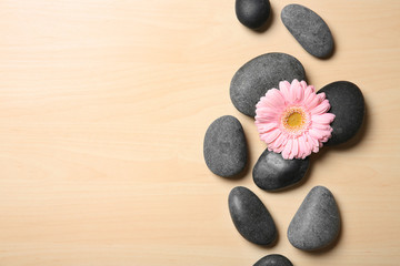 Spa stones with flower on wooden background, top view. Space for text