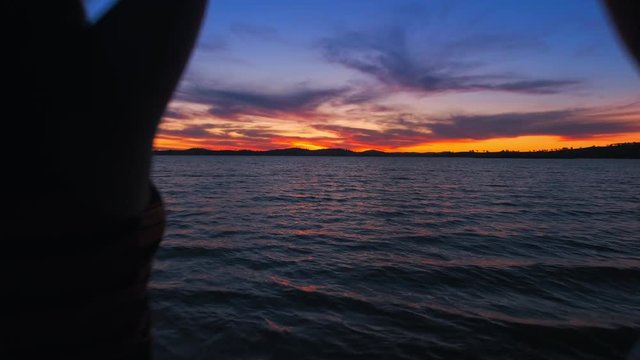 Dolly, shot of a two girls holding up their hands, standing on a beach, sunset in the background, at lake Huma, on a sunny evening dusk, at Hume Reservoir, New South Wales, Australia -  slow motion