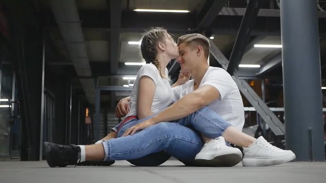 A young couple sits on the floor of the station and laughs, grimacing fun and funny.
