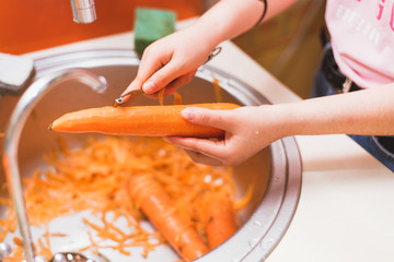 The girl cleans carrots from dirt and skins in the sink under the faucet. cleaning carrots in the sink.