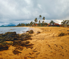 Cloudy evening view of Maenam beach, Koh Samui, Thailand. Beautiful seascape with sea waves and rocks scattered on beach sand. Rainy ominous grey storm clouds - dramatic sky.