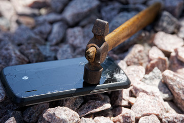 Broken glass of smartphone with hammer on gravel stones. Selective focus
