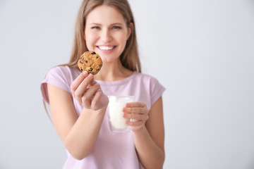 Beautiful young woman with tasty cookie and glass of milk on light background