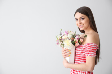 Beautiful young woman with bouquet of flowers on light background