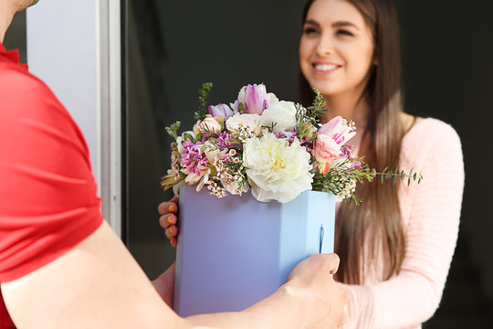 Young woman receiving beautiful flowers from delivery man at home