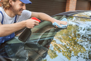 Male worker cleaning car window after applying tinting foil outdoors