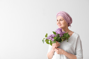 Mature woman after chemotherapy with bouquet of flowers on light background