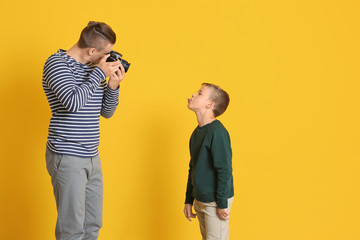 Father taking photo of his little son on color background