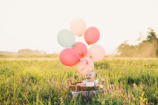 Baby girl in wicker basket with balloons on nature at summer