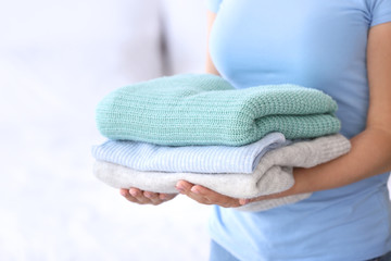 Young woman with stack of clean clothes at home, closeup