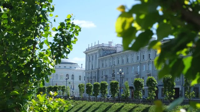 Close-up view of green leaves with Chernoyarovsky Passage, on the background in summer day. Stock footage. Kazan city, Tatarstan republic, Kremlevskaya street