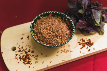 Zira rice lies in an oriental plate. dark rice lies on an oriental background, a golden tablecloth, a wooden cutting board next to basil.
