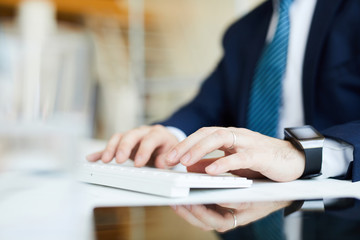 Close-up of unrecognizable businessman in suit sitting at desk and typing on keyboard while preparing business plan on computer
