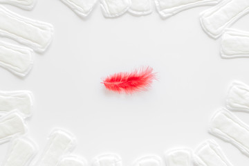Menstruation calendar concept with sanitary pads and feather on white background top view