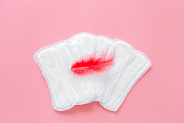 Menstruation calendar concept with sanitary pads and feather on pink background top view