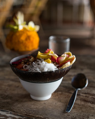 smoothie bowl in a coconut shell plate with with strawberries, chia seeds, banana, granola, flower on wooden background
