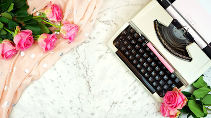 Romantic vintage feminine writing scene with old typewriter and pink roses on marble table with...