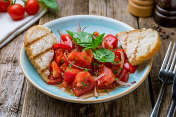 Tomato salad with red onion and bread on wooden table