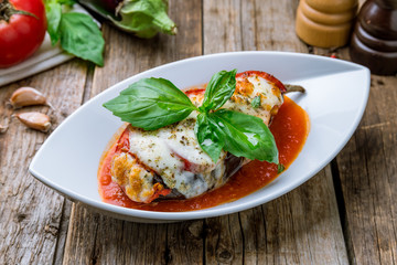 Parmigiano eggplant with basyl on white plate on wooden background