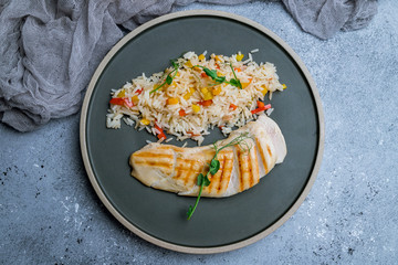 sliced Grilled chicken Breasts with rice and vegetables on grey plate