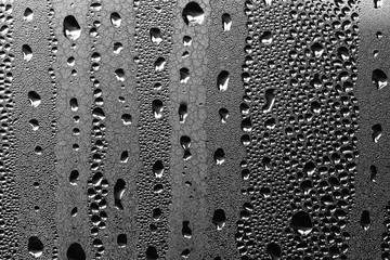 Water running down glass window at night. Dark background with white silver drops of rain or condensation
