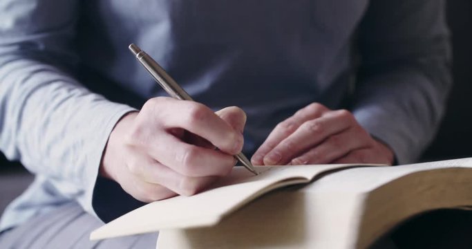 Handheld closeup shot of a woman studying the Bible at home and taking notes.