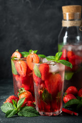 Fresh lemonade with ice, mint and strawberry on top in glass on black table background. Cold summer drink. Sparkling glasses with berry cocktail