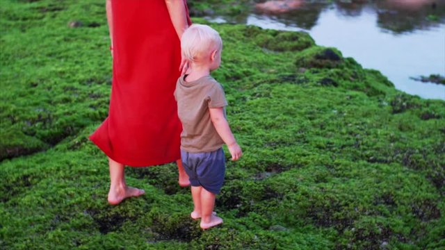 Barefooted caucasian mother and son are walking carefully on green algae at low tide. Slow motion. Famous Balangan beach, Bali, Indonesia