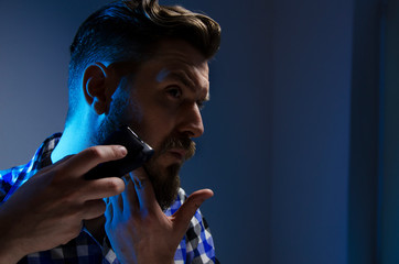 Studio shot, closeup of man shaving beard with electric shaver , dark background 