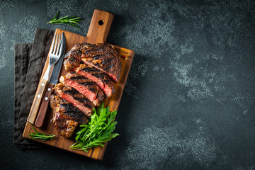 Sliced steak ribeye, grilled with pepper, garlic, salt and thyme served on a wooden cutting Board on a dark stone background. Top view with copy space. Flat lay - obrazy, fototapety, plakaty