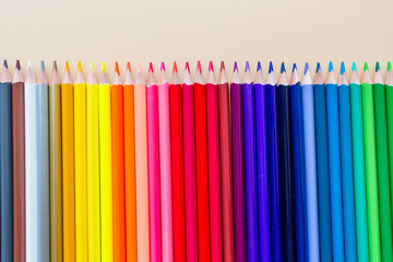 Bright and colorful background with many crayons lying on pastel orange paper. Top view, flat lay, mockup, overhead, copy space. Education and back to school concept