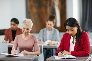 Group of adult students taking notes in class during training course on business and management,...