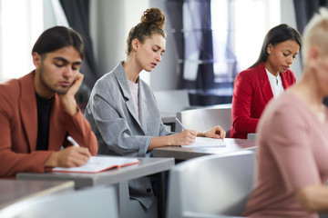 Side view at group of students taking notes in class during training course on business and management, copy space