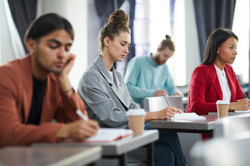 Side view portrait of contemporary young woman taking notes in class during training course on business and management, copy space