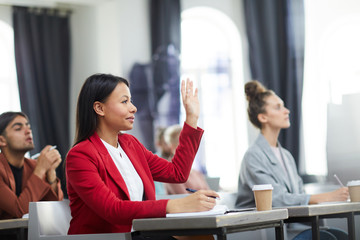 Side view portrait of smiling mixed-race businesswoman raising hand in class during training course on business and management, copy space