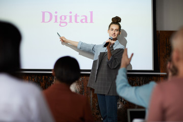 Portrait of contemporary young woman giving presentation pointing at word DIGITAL on projector...