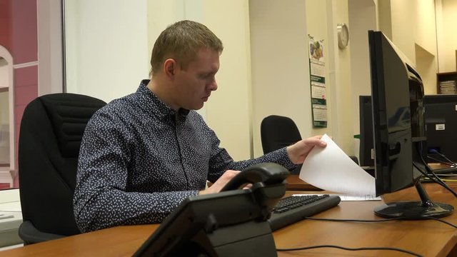 the guy is typing data on the computer from the documents lying on the table.