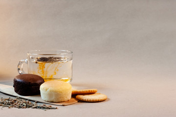 Cheese cakes, a cup of tea, crackers and dried tea leaves with spatula on paper. The tea in the cup is melted.  Sweetmeat concept. Choco and original flavor.