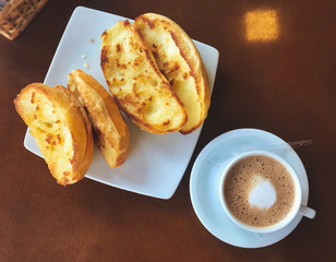Brazilian breakfast.  Capuccino cup and toasted bread with butter background.