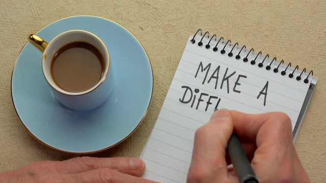 Make a difference - man hand writing a note with a black marker in a spiral notebook, overhead view
