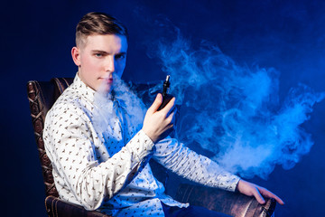 Vaping. Young man with a vape. A man blows smoke through the nostrils. A person smokes an electronic cigarette. The man looks intriguingly. The shrill male gaze. Beau. Dandy. Smoke break.