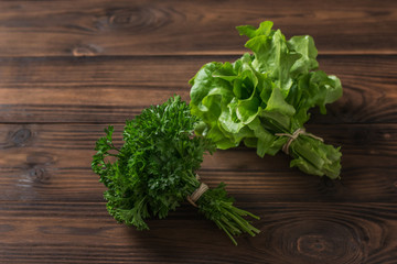 A bunch of parsley and a bunch of lettuce on a brown wooden table.